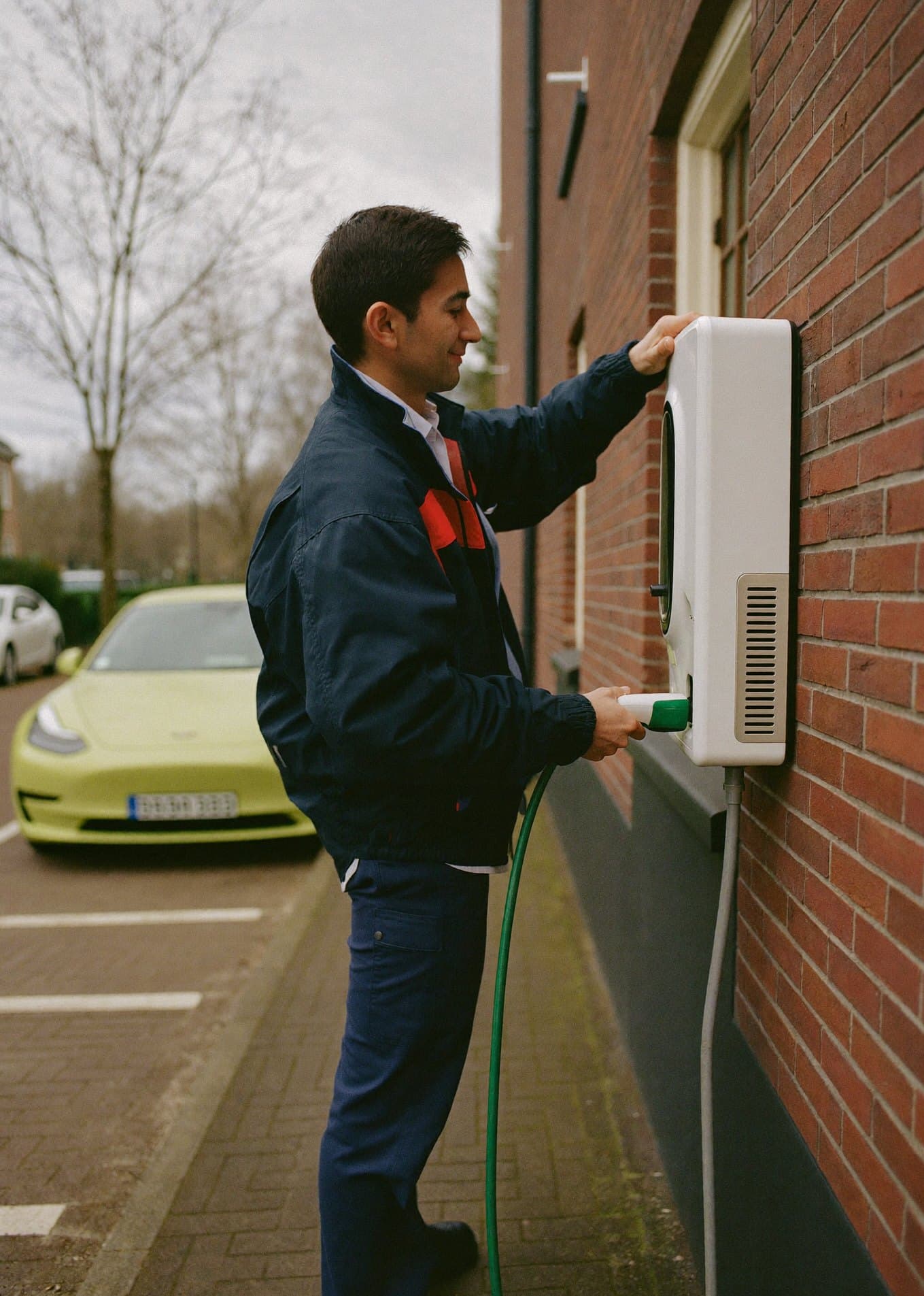 Een installateur sluit een laadpaal aan tegen de gevel van een woning